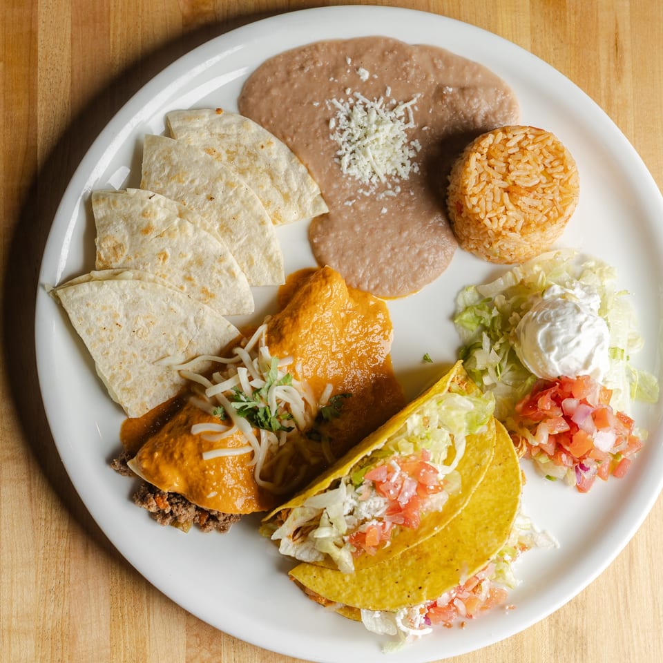 Mexican combination plate with tacos, enchiladas, refried beans, rice, tortillas, lettuce, and sour cream.