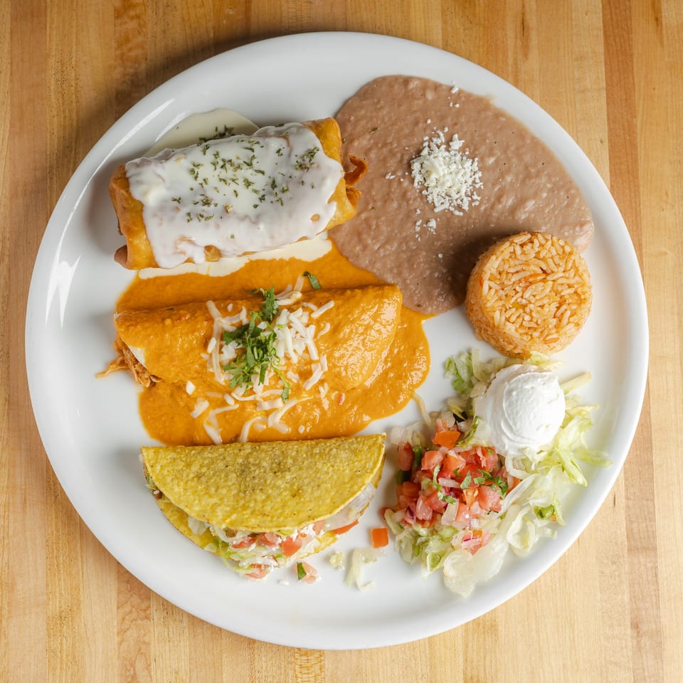 Mexican combination plate with enchiladas, refried beans, Spanish rice, taco, salad, and creamy toppings.