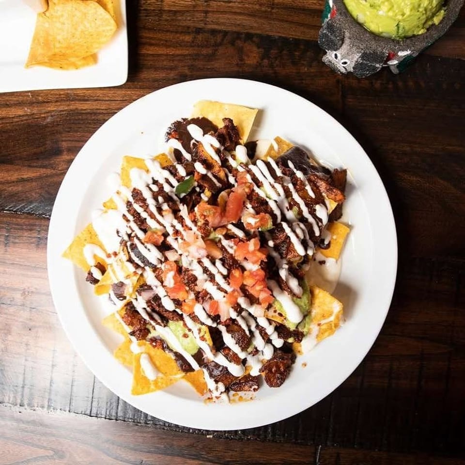 Loaded nachos topped with grilled meat, pico de gallo, guacamole, and creamy white sauce on a plate.