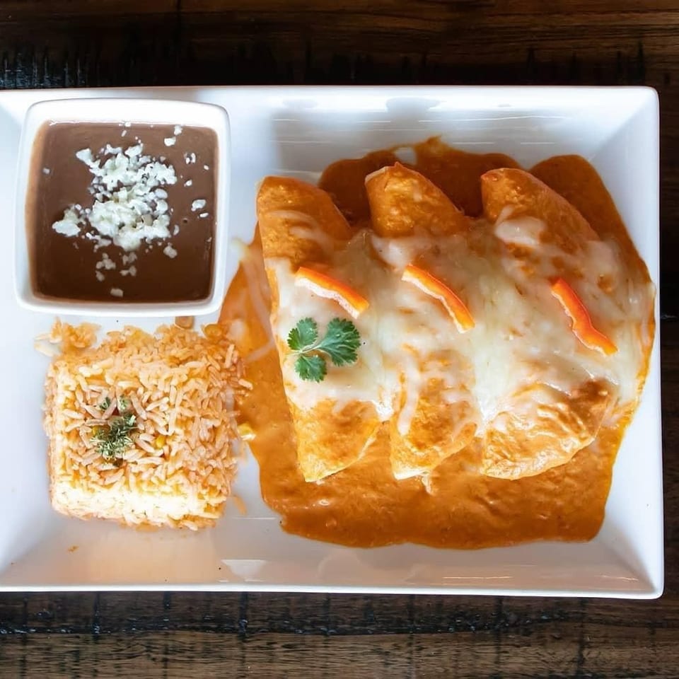 Three cheese-covered enchiladas in orange sauce served with Mexican rice and refried beans on a white plate.