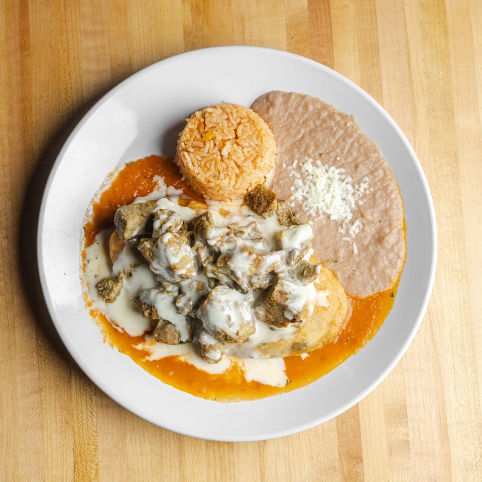 Plate of orange rice, refried beans, and grilled meat topped with creamy white sauce and red salsa.
