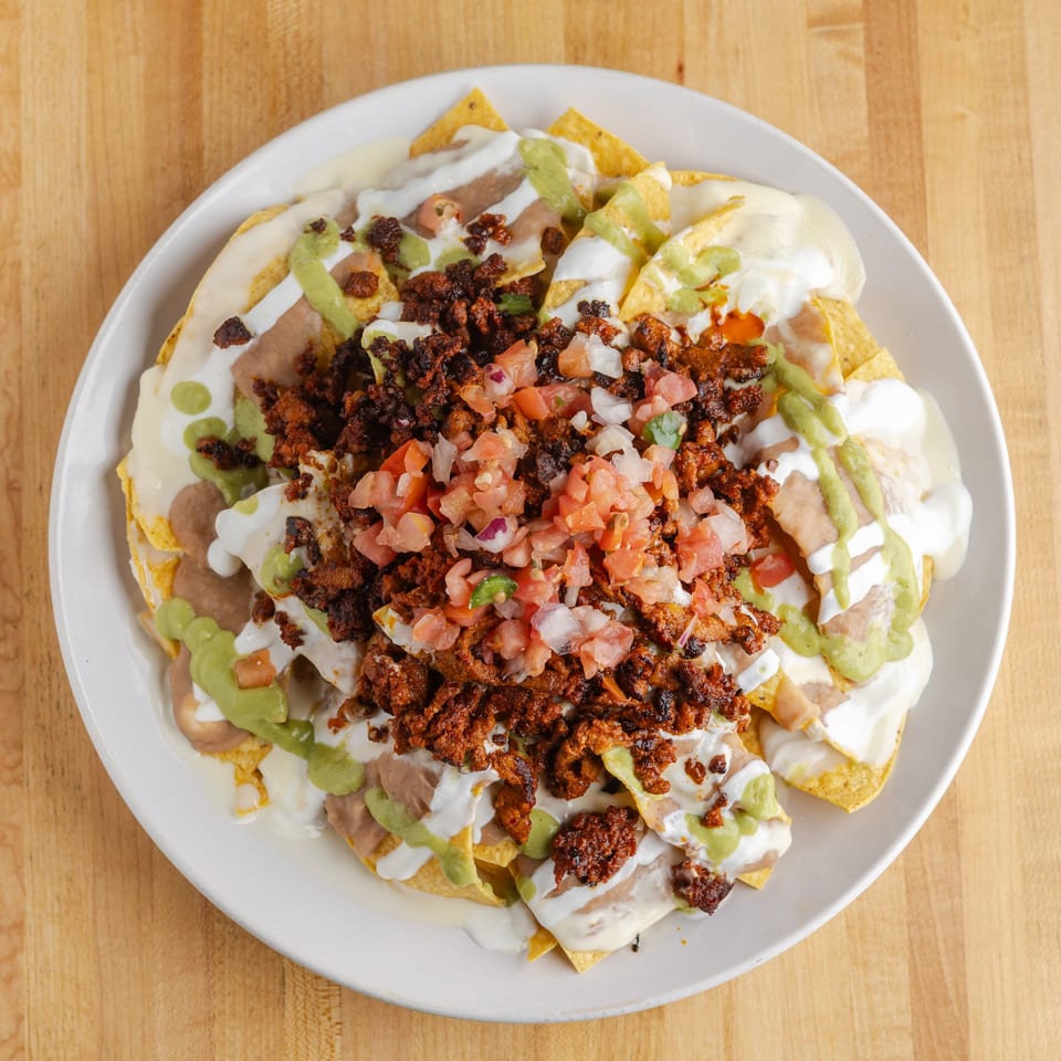 Loaded nachos topped with seasoned meat, beans, pico de gallo, guacamole, sour cream, and cheese on a white plate.