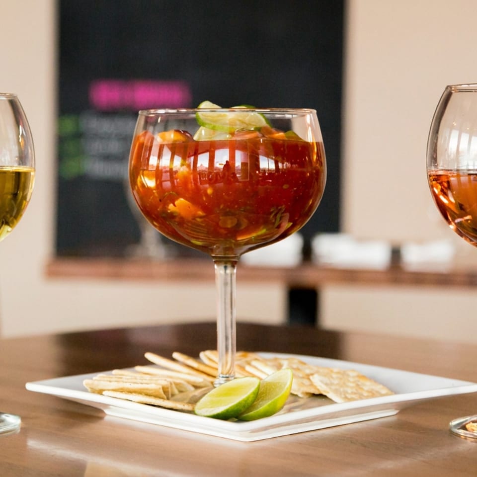 Three stemmed glasses of colorful cocktails surround a plate of tortilla chips and lime wedges on a restaurant table.