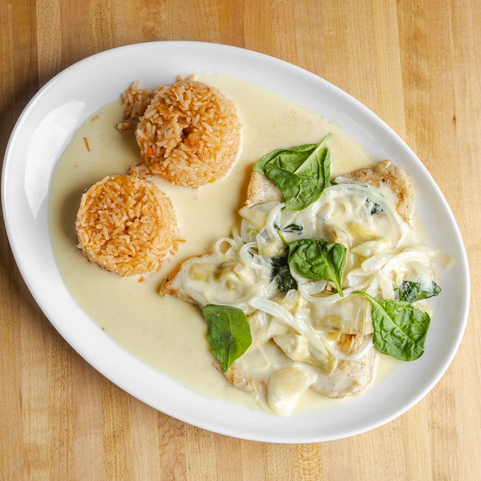 White plate of grilled chicken with creamy spinach sauce and two mounds of seasoned rice on a wooden table.