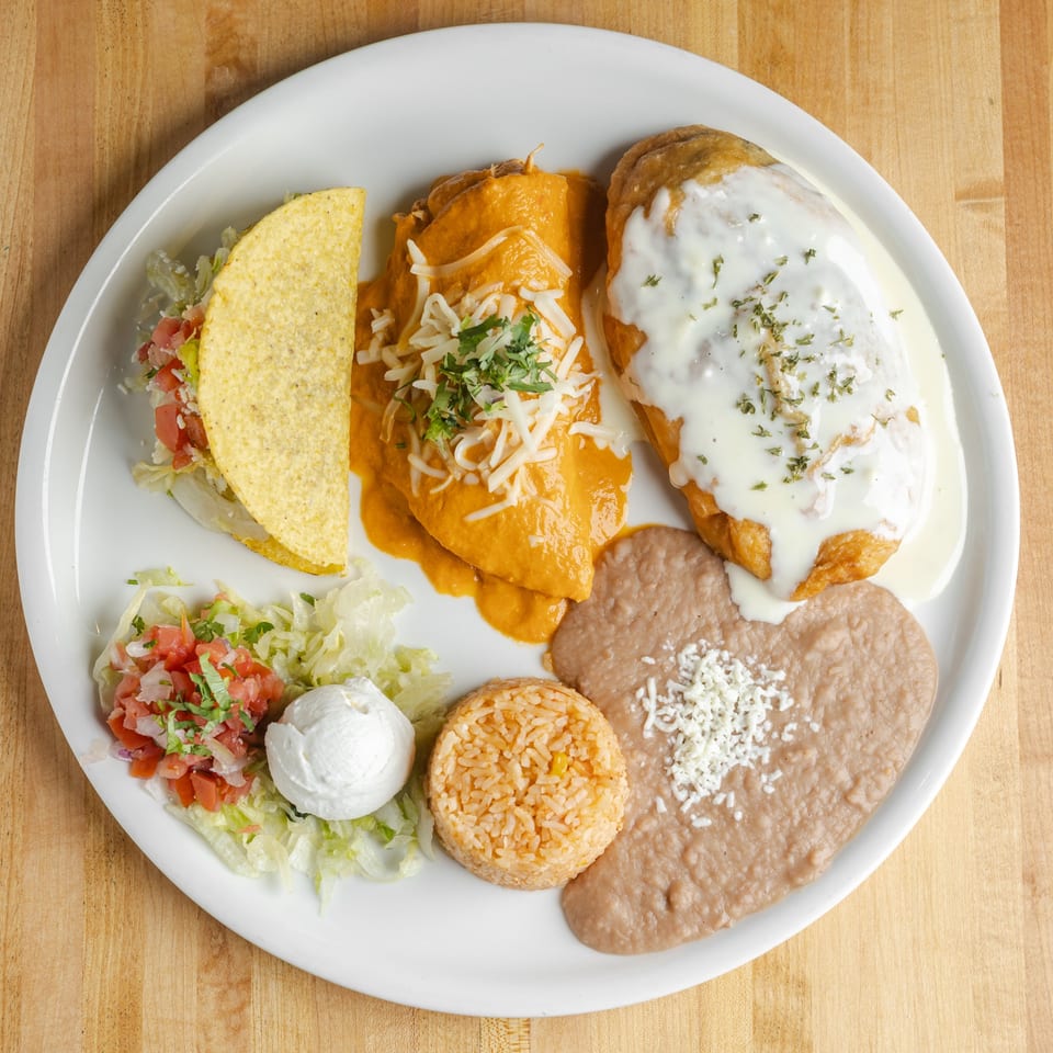 Mexican combination plate with tacos, enchiladas, a creamy-topped burrito, refried beans, rice, salad, salsa, and sour cream.