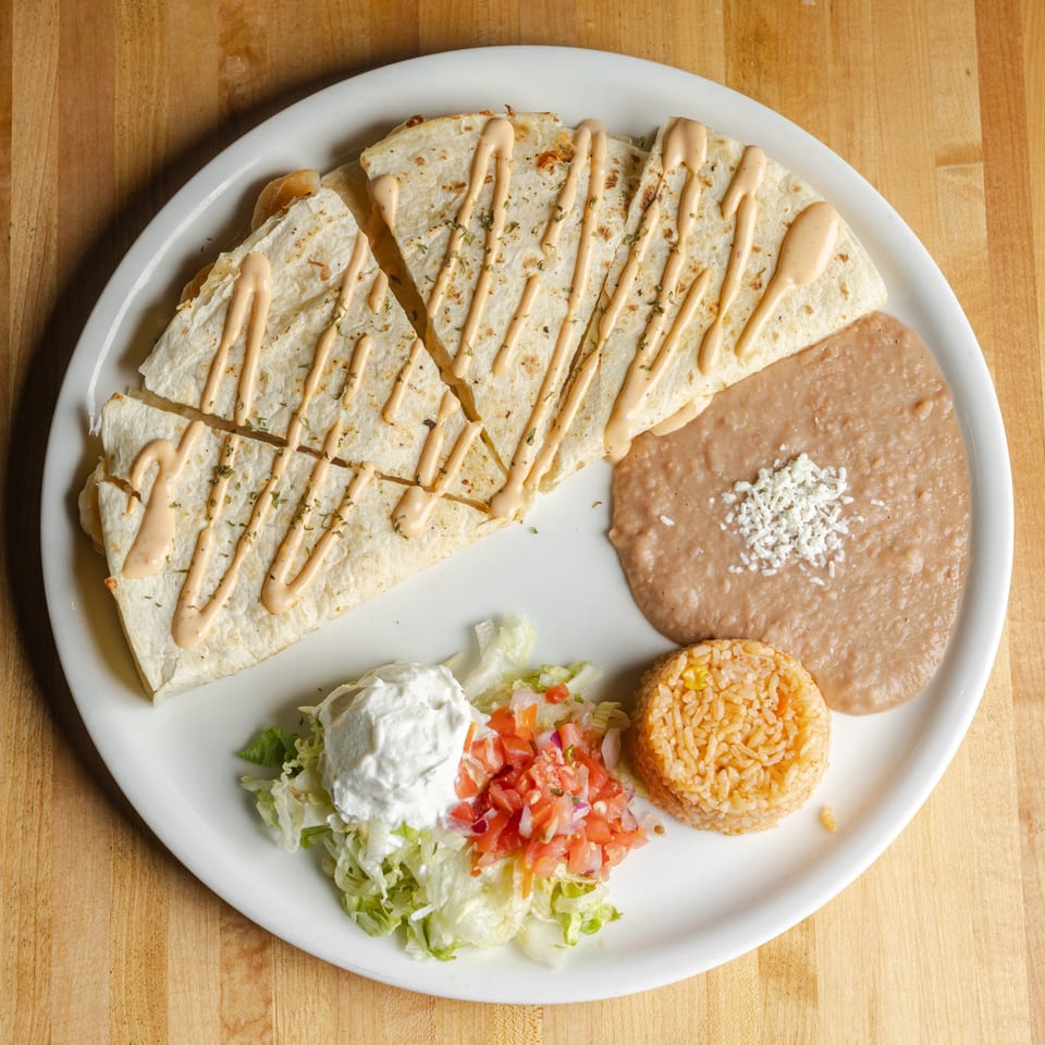 Mexican combo plate with sauced quesadilla slices, refried beans, Mexican rice, lettuce salad, sour cream, and pico de gallo.