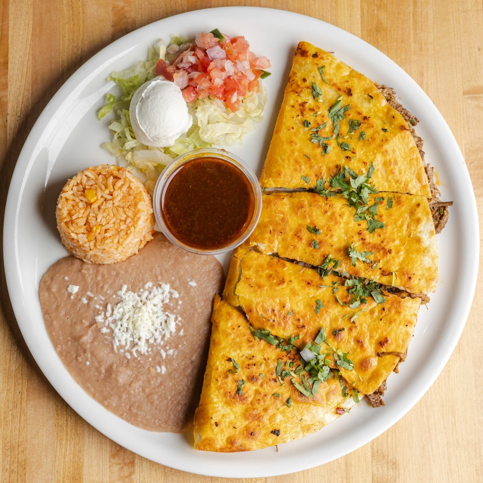Mexican platter with cheesy quesadillas, rice, refried beans, salad, sour cream, pico de gallo, and red sauce.