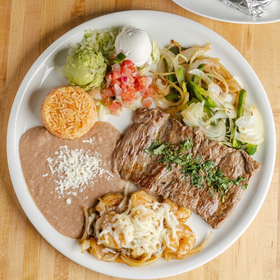 Mexican-style platter with grilled steak, rice, refried beans, sautéed vegetables, guacamole, pico de gallo, sour cream, and cheesy shrimp.